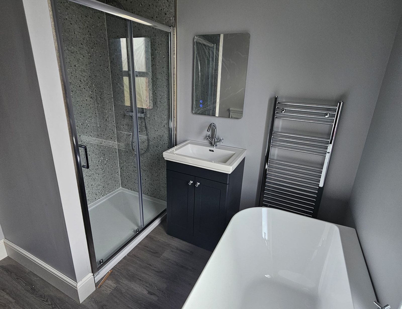 Finished bathroom with a freestanding bath, a glass shower enclosure, a navy vanity unit and a chrome towel radiator