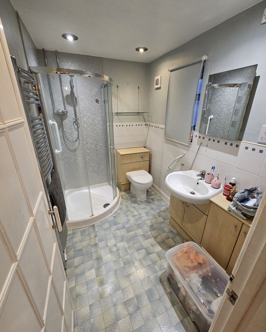 The old bathroom with a curved quadrant shower, a pine vanity unit and a tiled floor