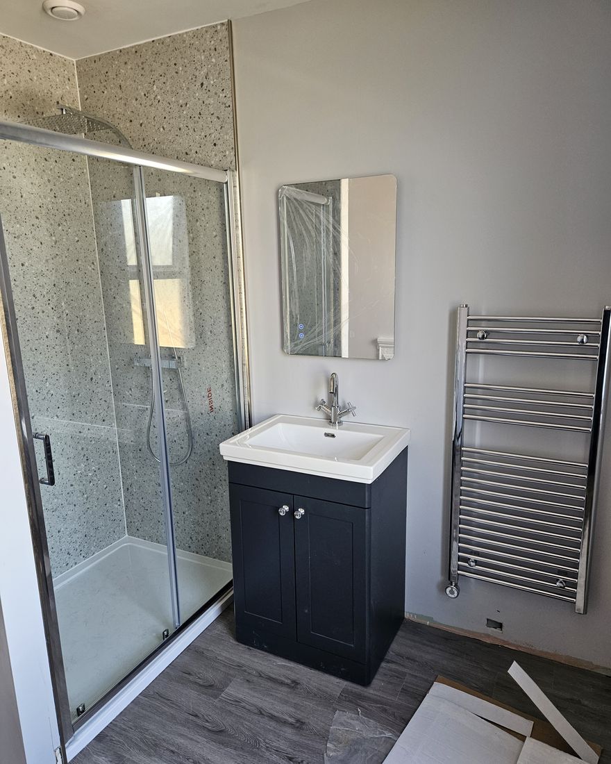 The finished shower enclosure, a navy vanity unit with a mirror above and a chrome towel radiator