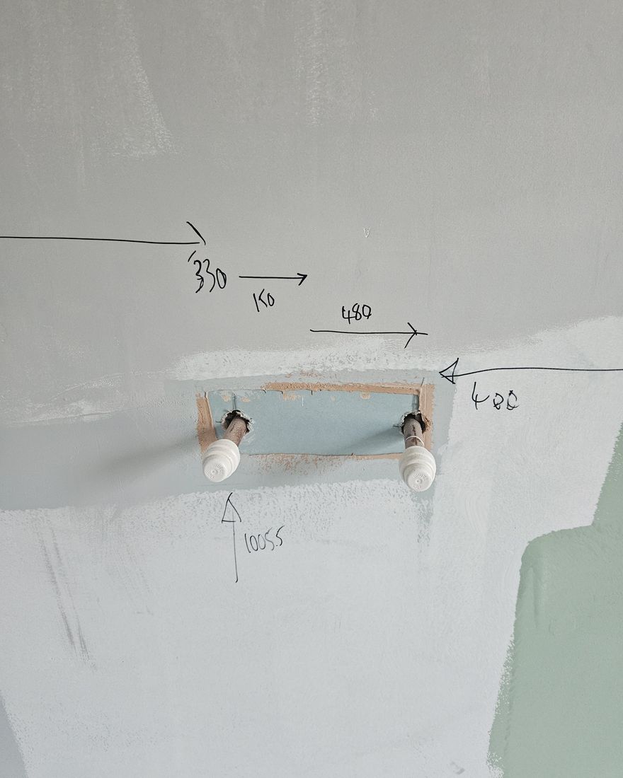 Two pipe tails set out in the wall for the basin, with pencil measurements marked around them