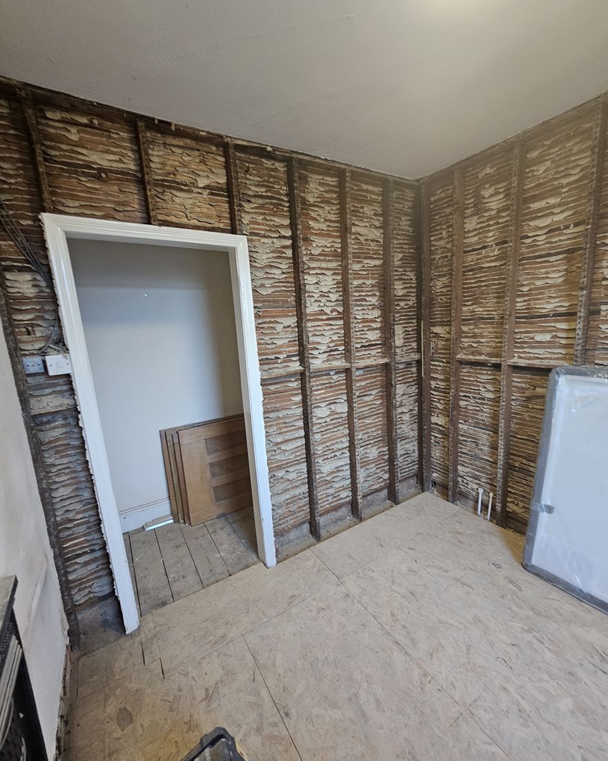 The bathroom walls stripped back to bare lath around the doorway, with a new ply floor