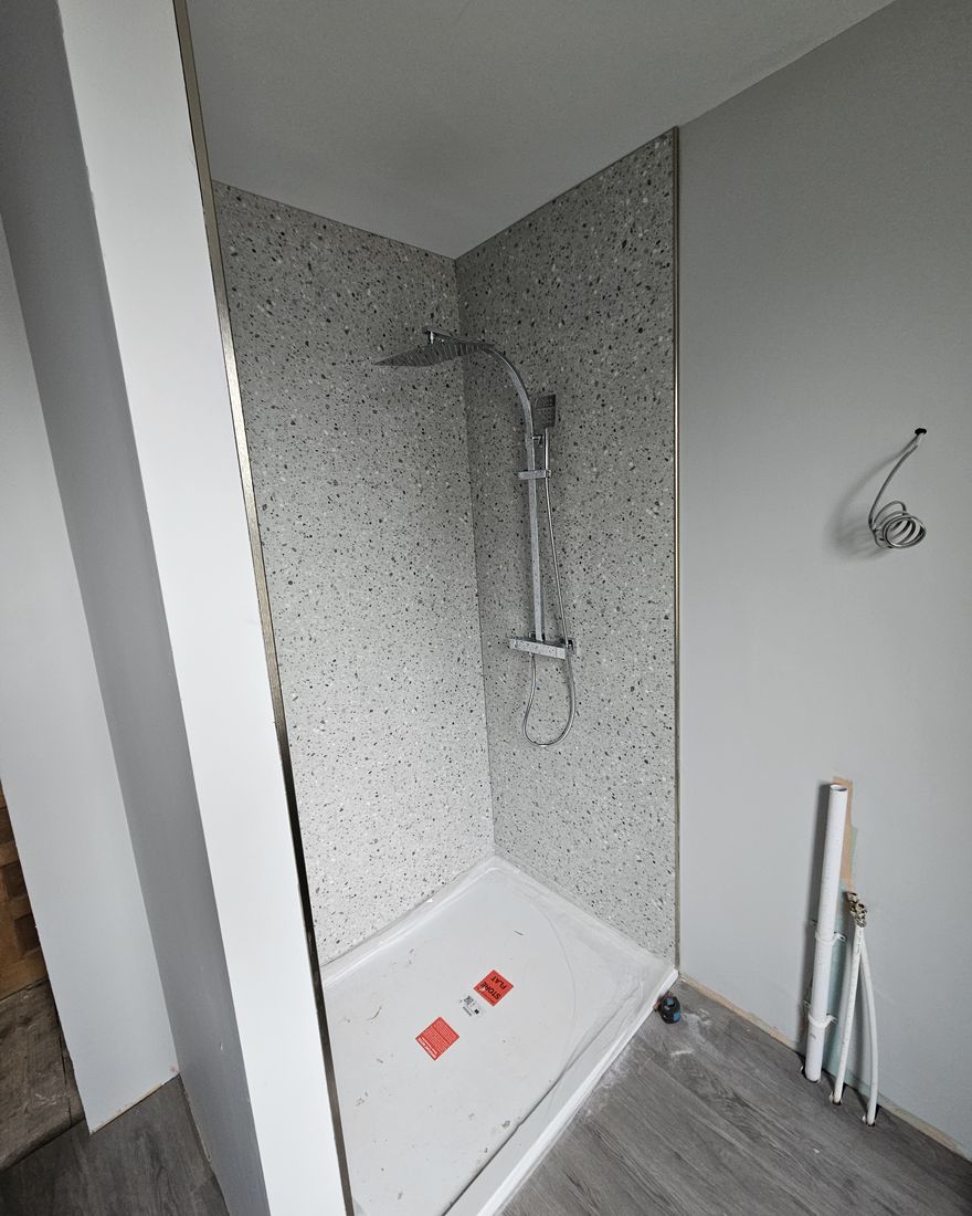 The shower area with a white tray, terrazzo-effect walls and a chrome rail shower fitted