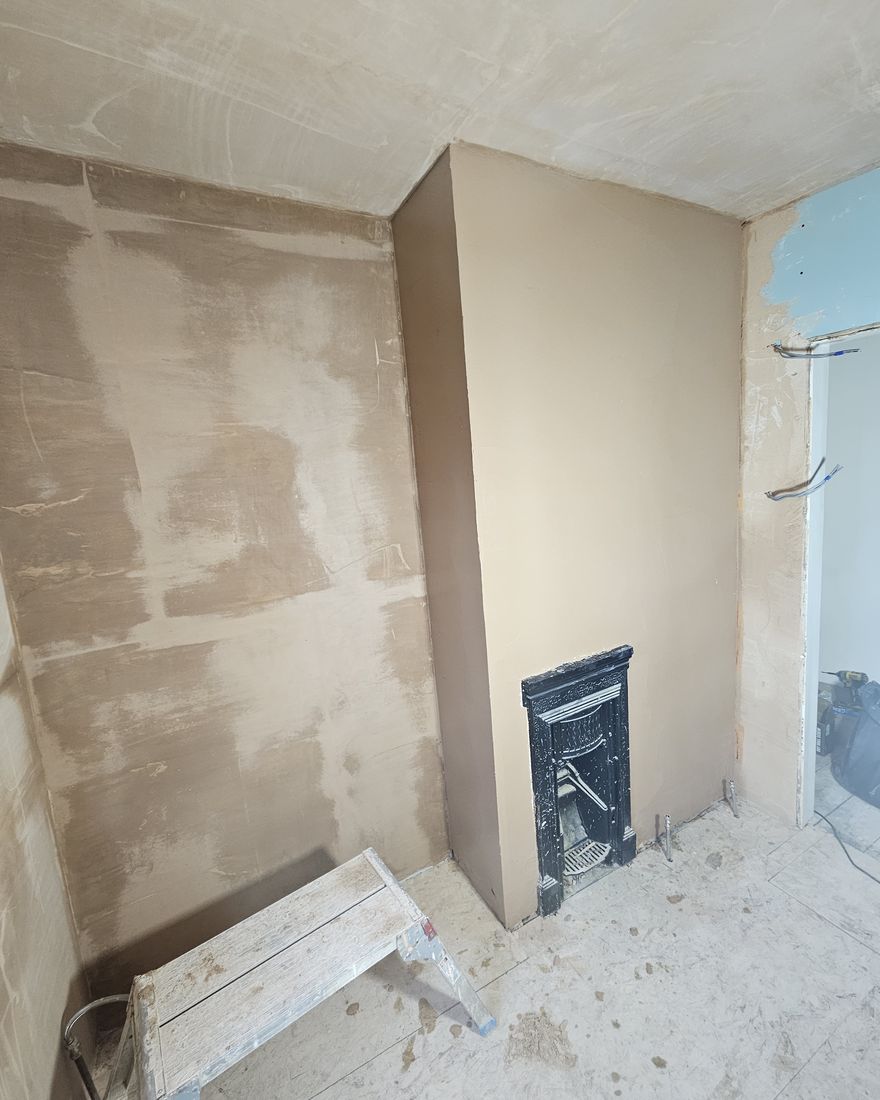 Freshly skimmed walls, the shower wall boxed in and a small cast-iron fireplace in the chimney breast