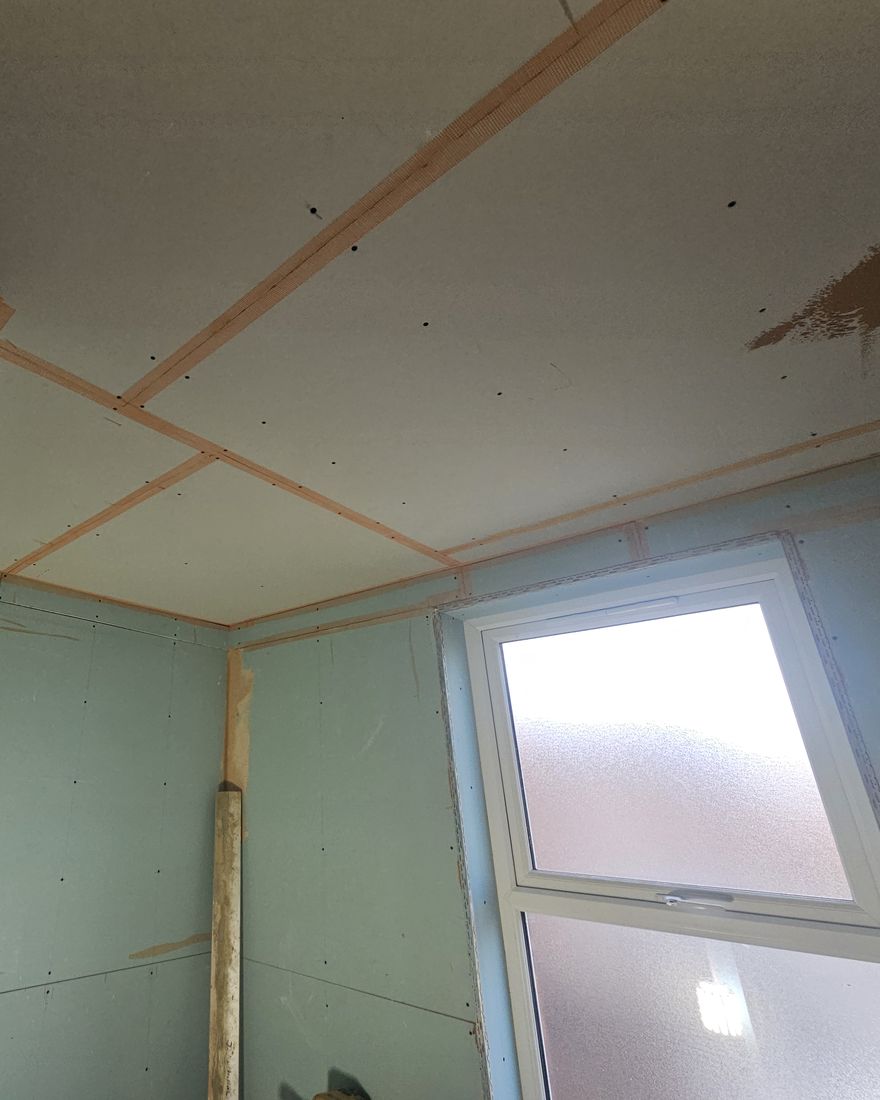Close view of the boarded bathroom ceiling with scrim tape over the board joints, above an obscured-glass window