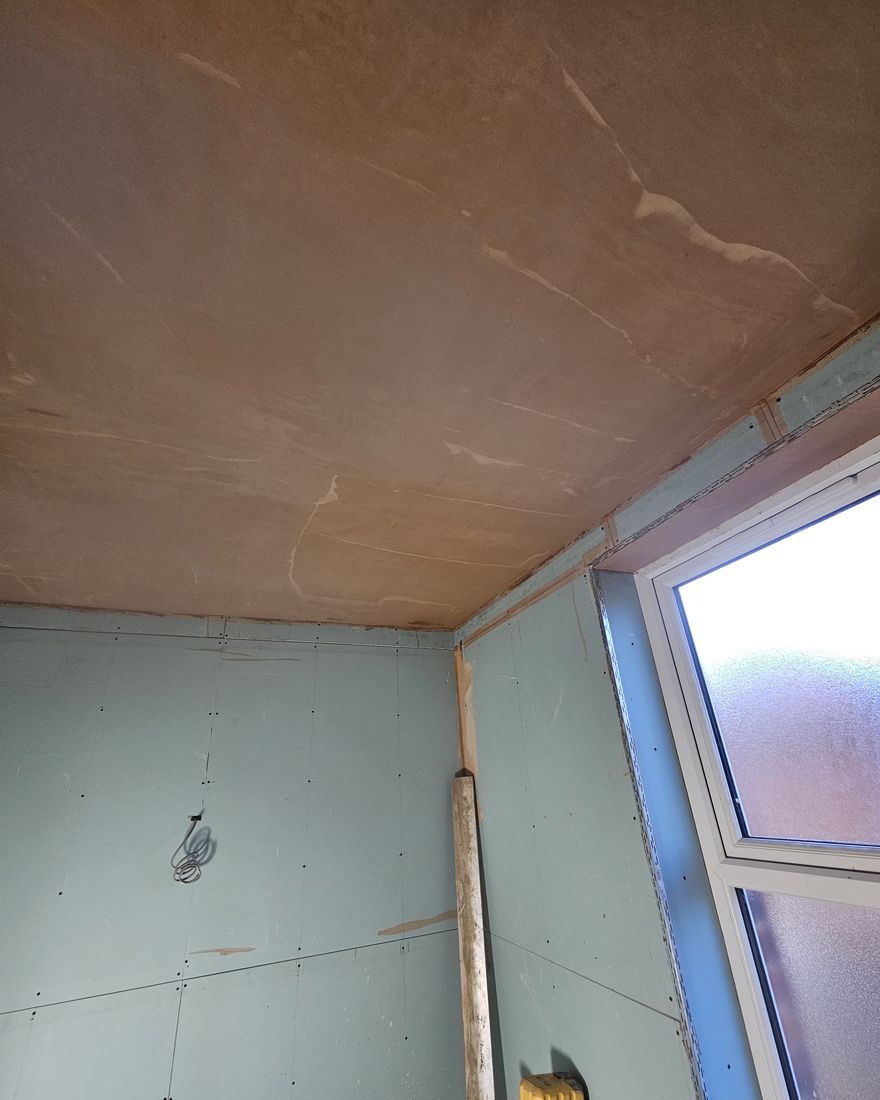 The bathroom ceiling freshly skimmed above an obscured-glass window, with the walls still boarded