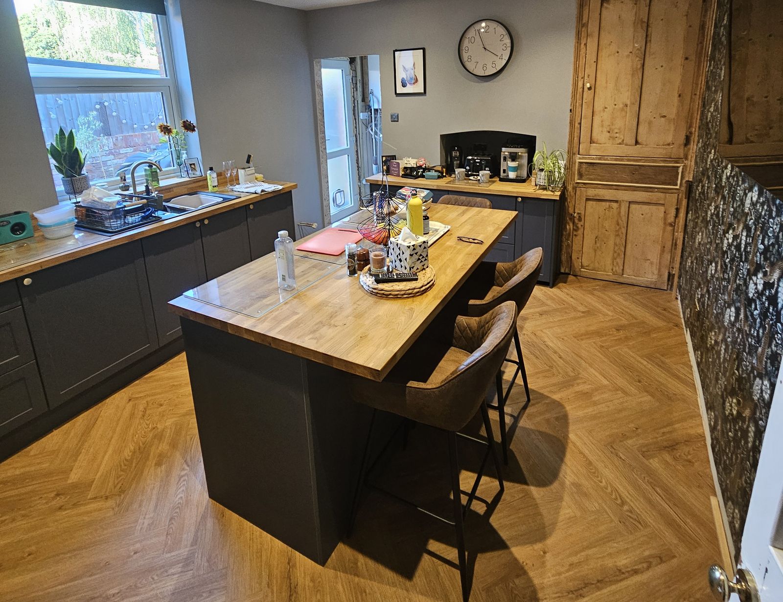 Finished kitchen-diner with dark grey units, oak worktops, an island with stools, a herringbone floor and an original pine larder door