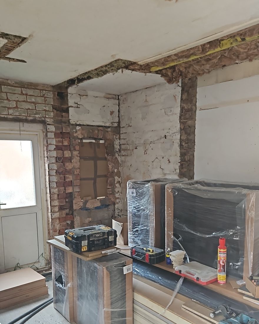 The kitchen during the works, with the original back wall opened up and bare brick showing around the opening, new units wrapped in protective film
