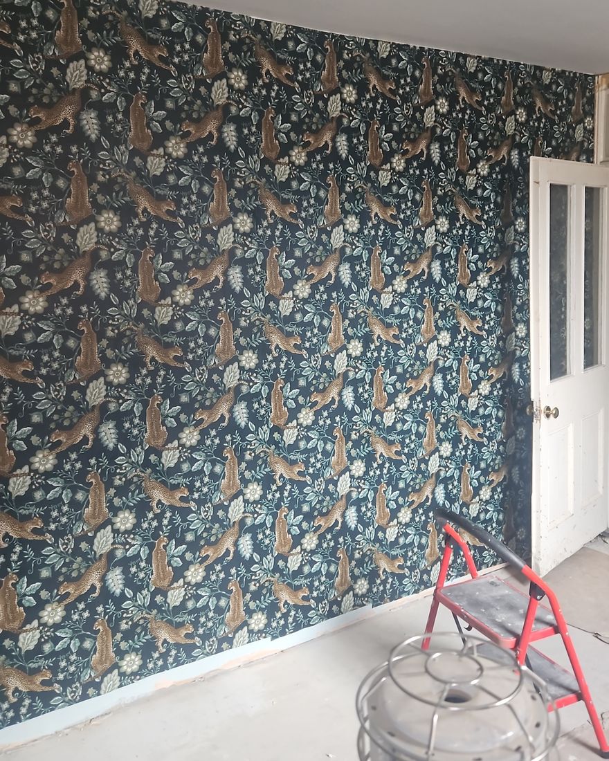 A newly hung dark botanical wallpaper on one wall beside a white panel door