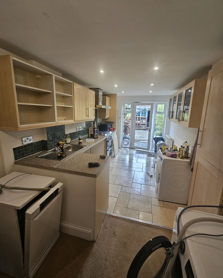 The old galley kitchen with pine-effect units and a tiled floor, looking towards French doors