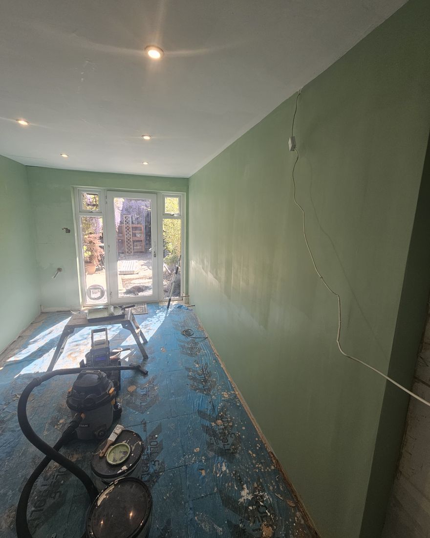 The empty galley kitchen painted sage green, with the floor protected, looking towards French doors