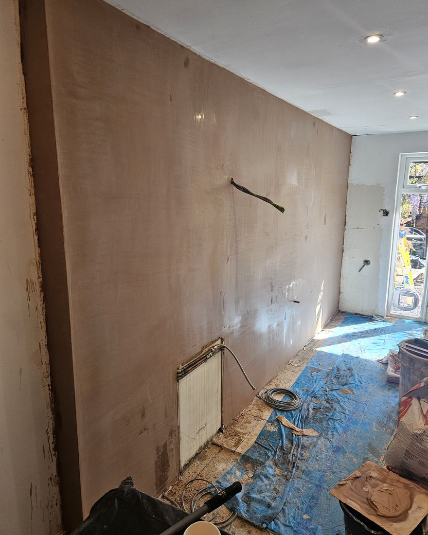 The long kitchen wall freshly plastered, with the floor protected