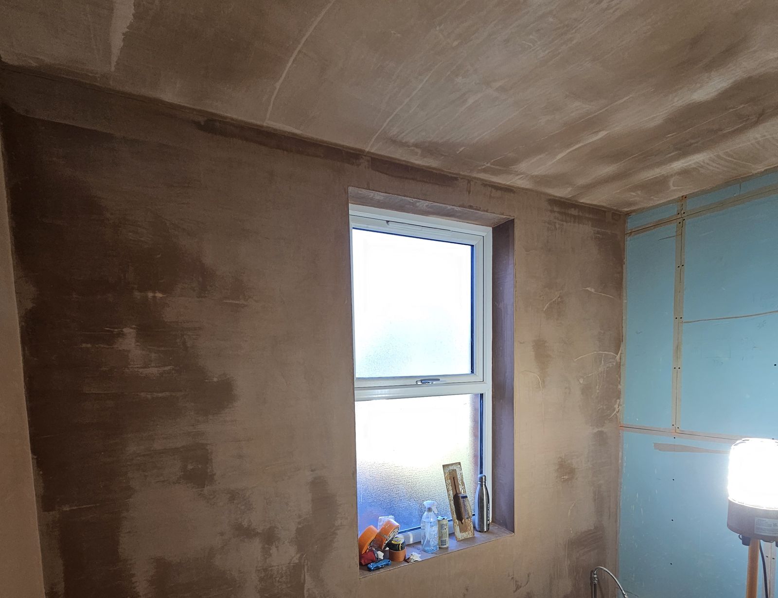 Bathroom with freshly skimmed walls and ceiling around an obscured-glass window, green moisture-resistant board on the right-hand wall
