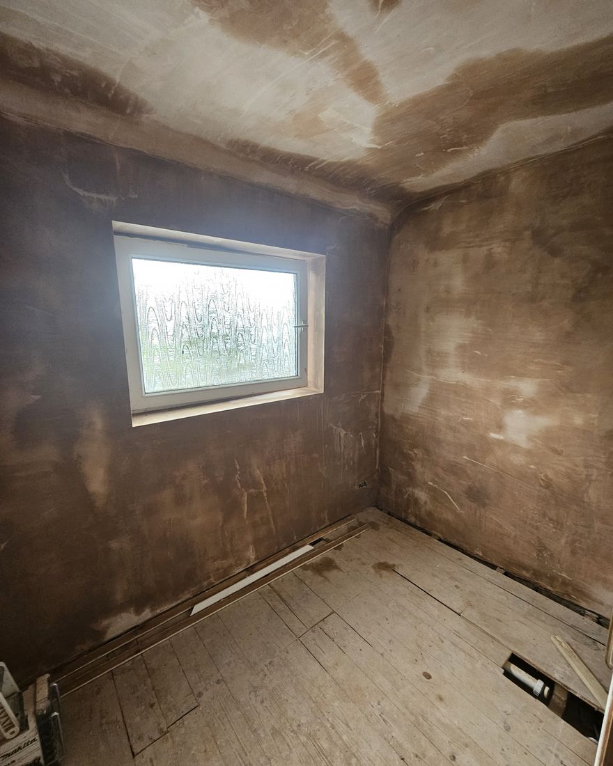 Small bathroom with walls and ceiling fully re-plastered and still drying, around an obscured-glass window