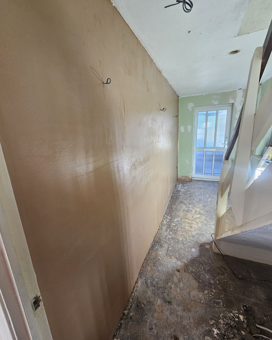 The same hallway wall freshly skimmed, with the back door at the end
