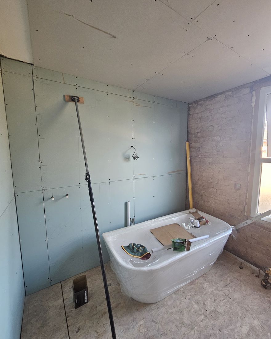 Bathroom walls and ceiling boarded in green moisture-resistant board, with a freestanding bath under protection
