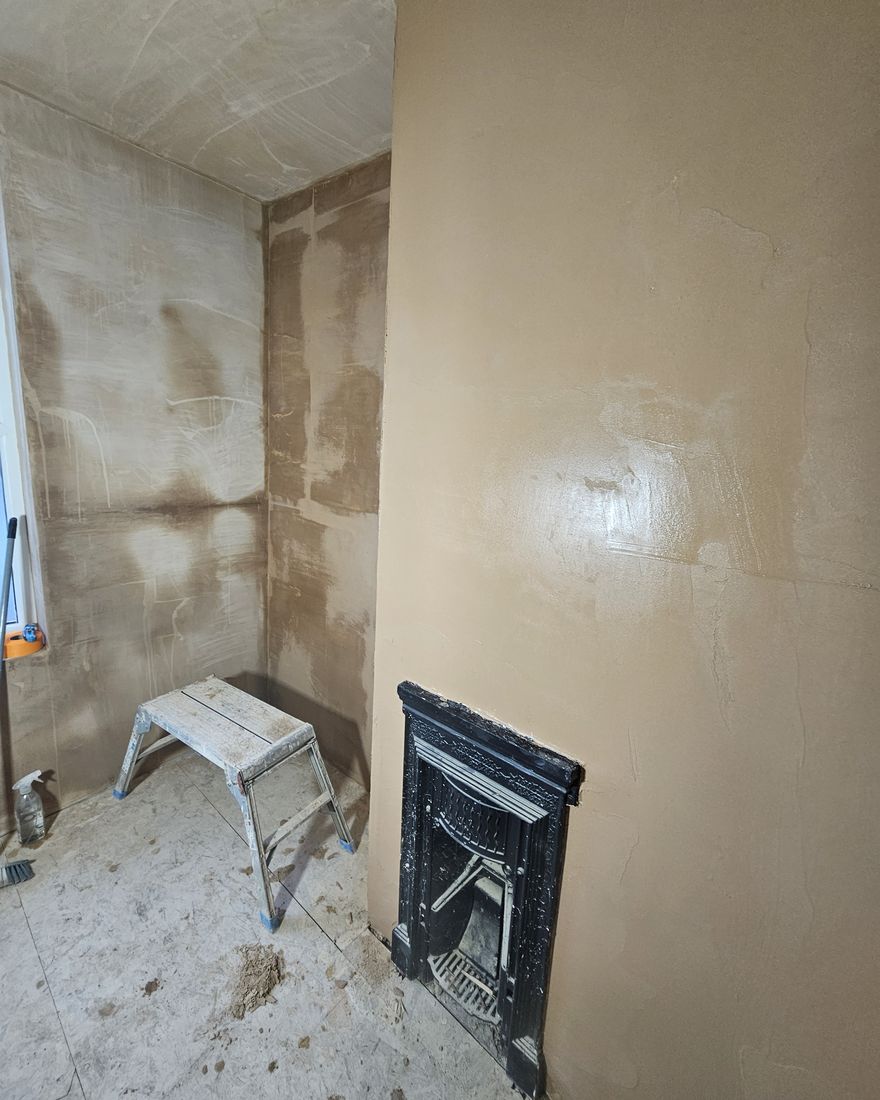 Small cast-iron fireplace in a freshly skimmed chimney breast, with a stepladder beside it