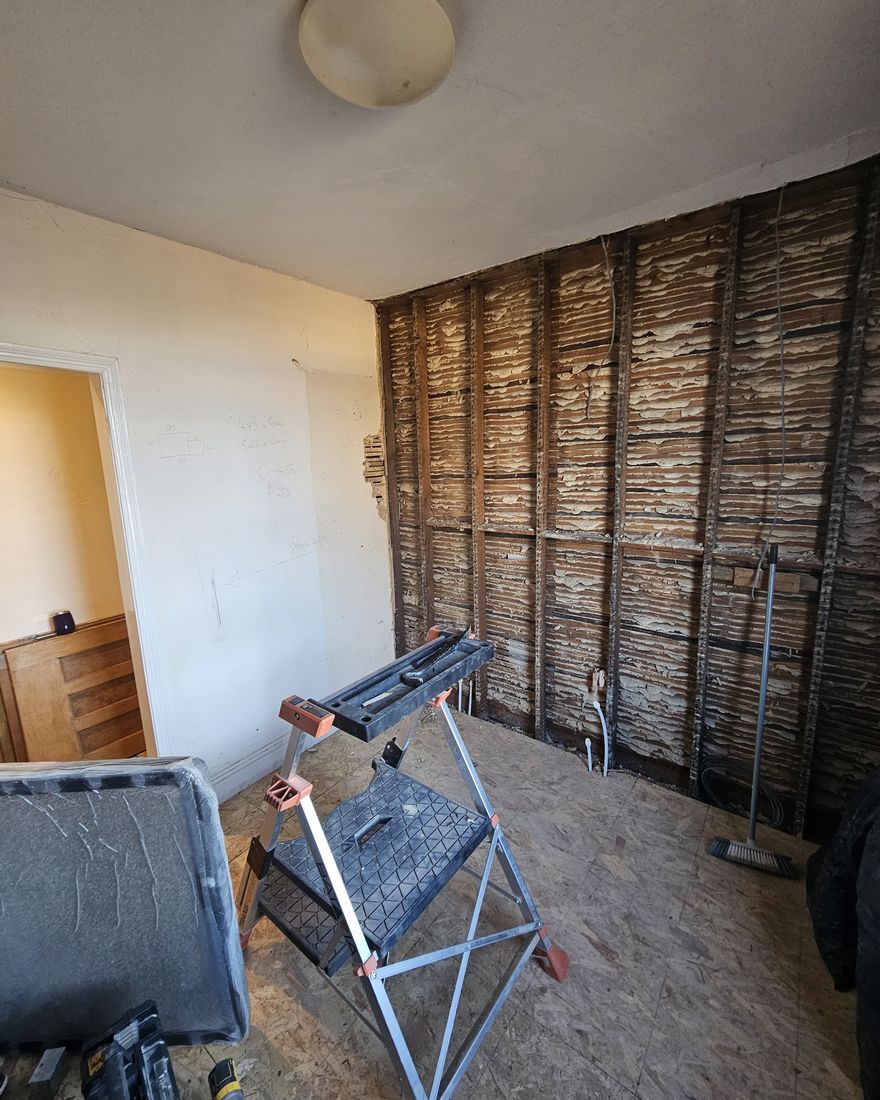 Wall stripped back to the timber lath, with a folding workbench in the room