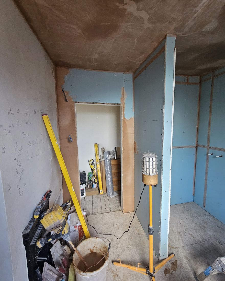 Skimming under way: the ceiling skimmed and the walls still boarded, with a work light and mixing tub