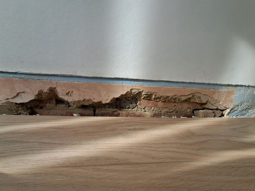Plaster cut back along the base of a wall, exposing the brickwork above the floor