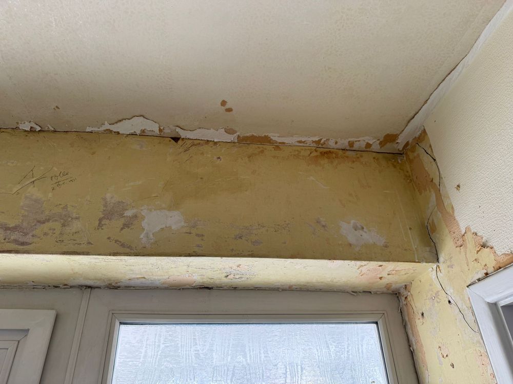 Stained, flaking plaster and paint above a white window frame