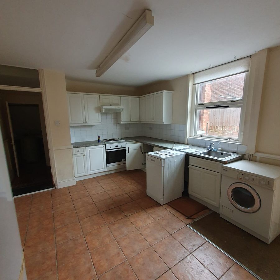 Dated white kitchen with terracotta floor tiles and a fluorescent strip light