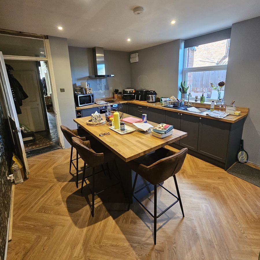 Finished kitchen-diner with a dining table and stools, dark units under the window and a herringbone floor