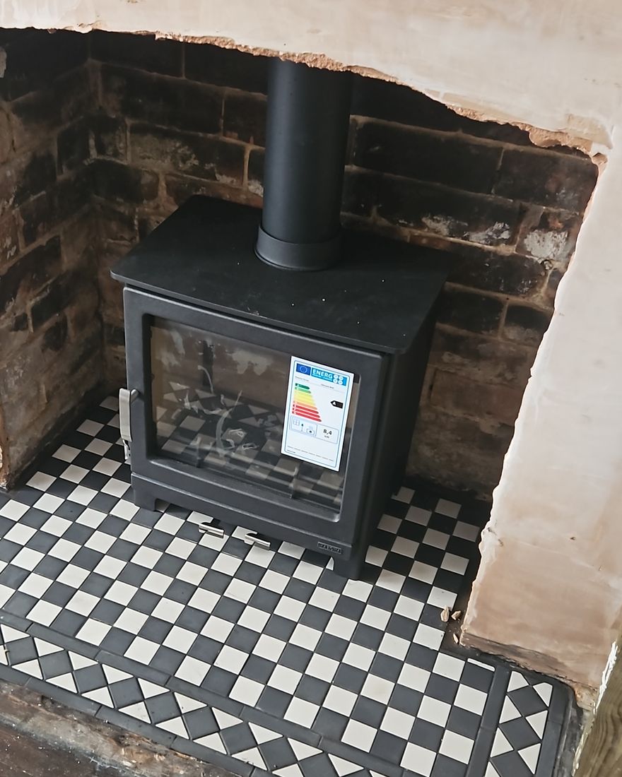 Black stove standing on a new black-and-white chequer tiled hearth in the opened brick fireplace