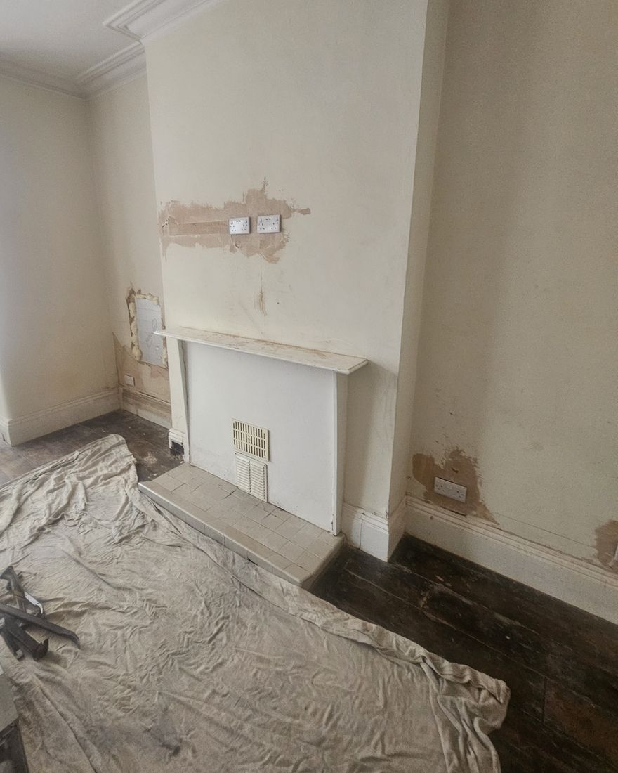 Chimney breast with an old painted fire surround and patch repairs, dust sheets on the floor