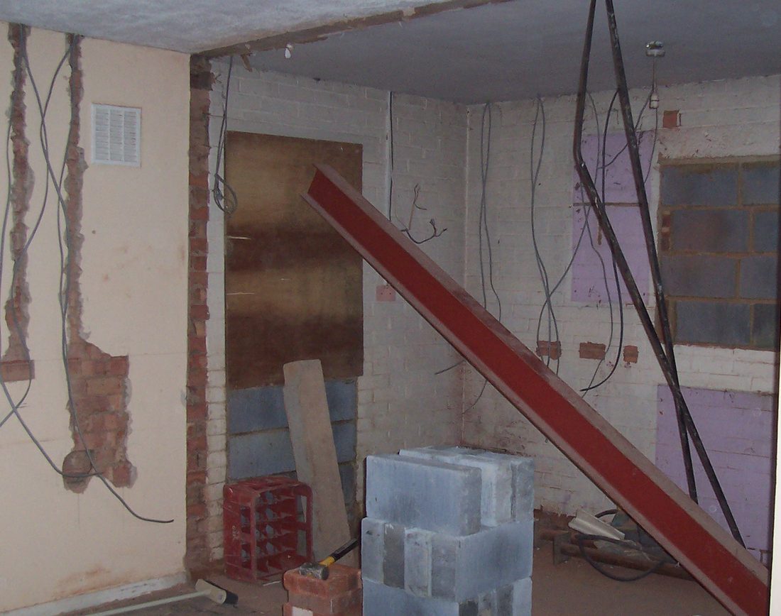 A red steel beam and stacked concrete blocks inside a room that is being opened up